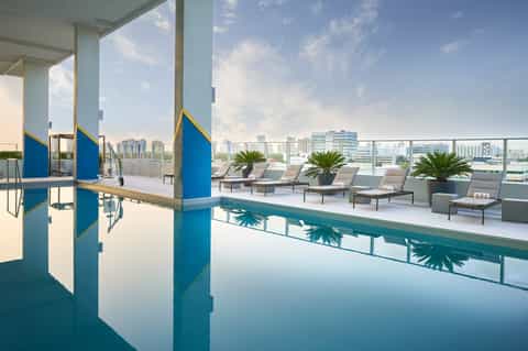 Indoor lap pool with city skyline views, lounge chairs, and palm plants on terrace