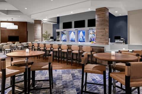 Modern resort lounge with wood furnishings, leather seating, bar with glass beverage coolers, and ambient lighting