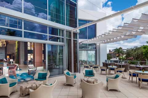 Modern rooftop terrace with white wicker chairs, pergola, and floor-to-ceiling glass doors