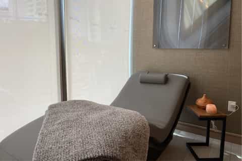 Modern spa treatment room with gray massage chair, floor-to-ceiling windows, and minimalist decor