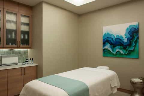 Spa treatment room with massage bed, wooden cabinets, skylight, and abstract blue-green artwork