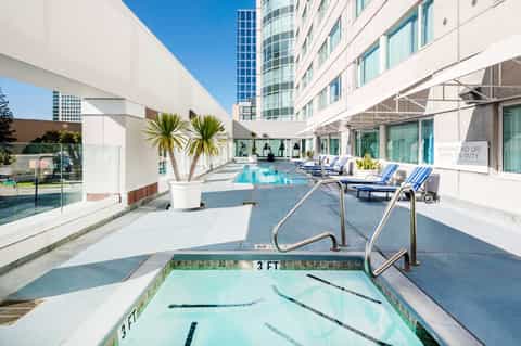 Modern hotel rooftop pool deck with lap pool, loungers, and city skyline views