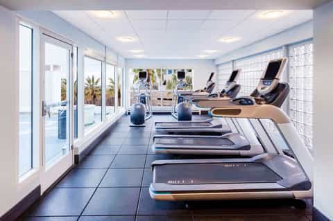 Modern fitness center with treadmills, stationary bikes, and floor-to-ceiling windows overlooking the ocean