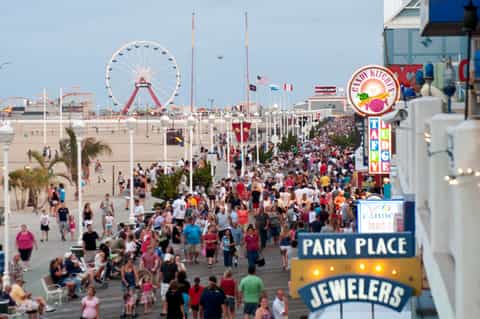 Crowded beachfront boardwalk with Ferris wheel and amusement park attractions visible