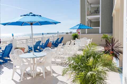 Beachfront deck with white Adirondack chairs, blue umbrellas, and ocean view at resort