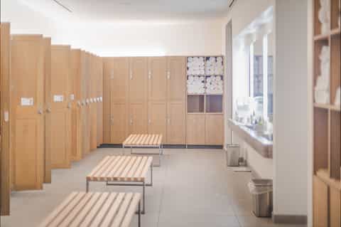 Clean locker room with wooden lockers, benches, and storage shelves with rolled towels