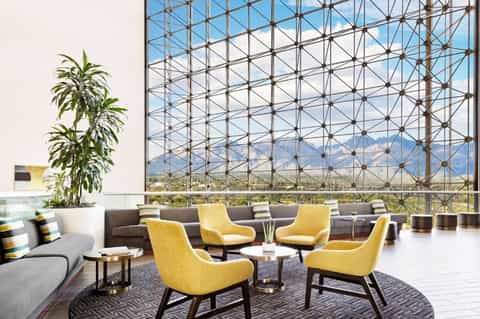 Modern lounge with yellow chairs, gray sofa, and floor-to-ceiling windows overlooking mountains