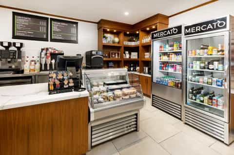Hotel café interior with wooden accents, display cases, refrigerated beverage coolers, and menu boards