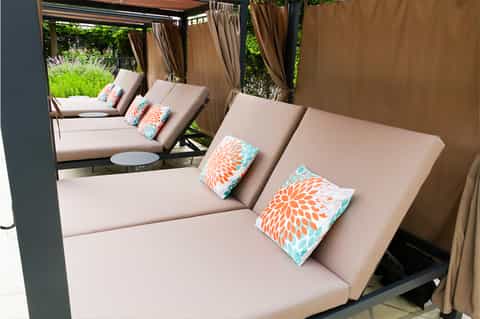 Luxury outdoor cabanas with beige cushions, colorful pillows, and tan curtains surrounding a pool area