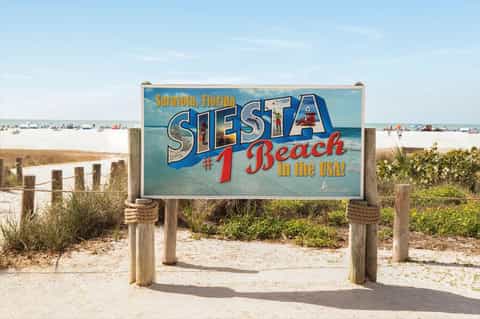 Siesta Beach sign in Sarasota, Florida, marking the #1 beach in the USA with sandy beach and ocean in background