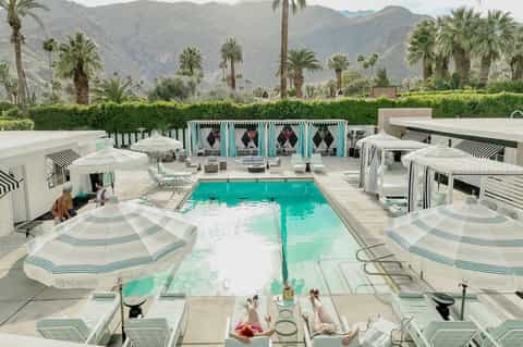 Turquoise resort pool surrounded by white lounge chairs with mountain backdrop and palm trees