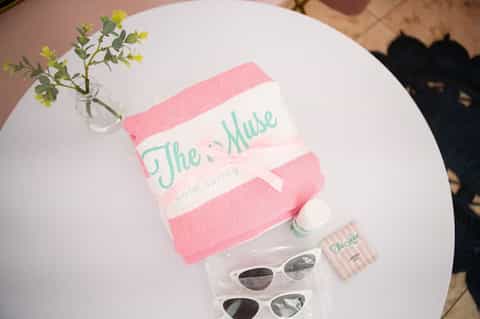 White table with pink towel branded 'The Muse', sunglasses, and small toiletries on display