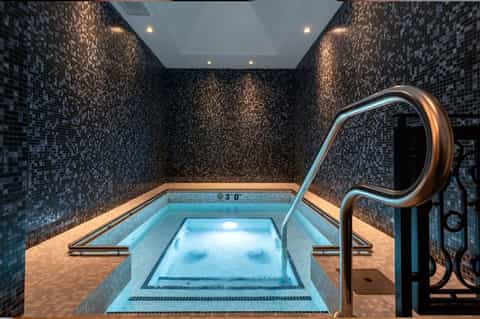 Luxurious indoor spa pool with mosaic tile walls, underwater lighting, and metal handrails