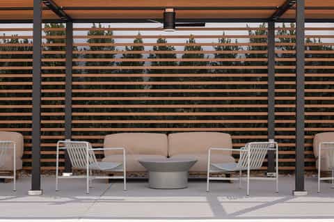 Modern outdoor patio with beige sofa, white chairs, and horizontal wood slat privacy screen