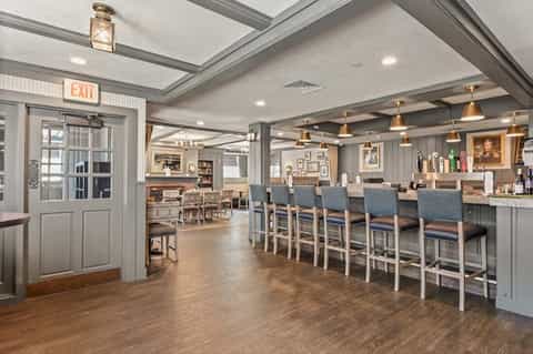 Hotel bar and lounge with gray ceiling, wooden floors, brass pendant lights, and blue bar stools