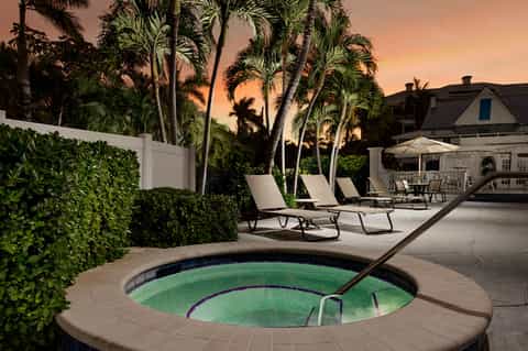 Spa hot tub at dusk surrounded by lounge chairs, palm trees, and modern residential architecture at sunset