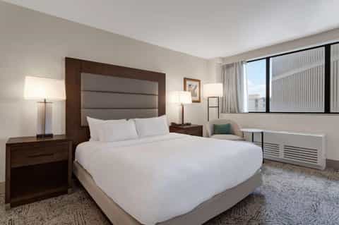 Modern hotel room with dark wood headboard, white bedding, and city view