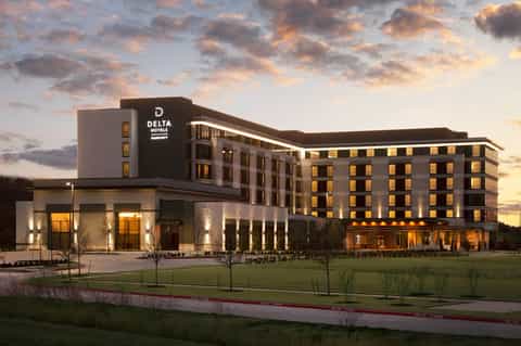 Modern Delta Hotels building exterior at dusk with illuminated windows and manicured landscape