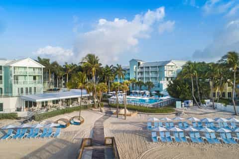 Aerial view of beachfront resort with palm trees, pools, and blue lounge chairs