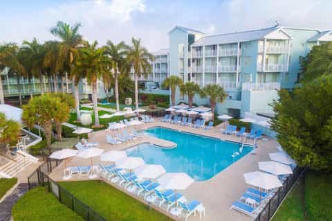 Aerial view of resort pool surrounded by palm trees, colorful buildings, and lounge chairs