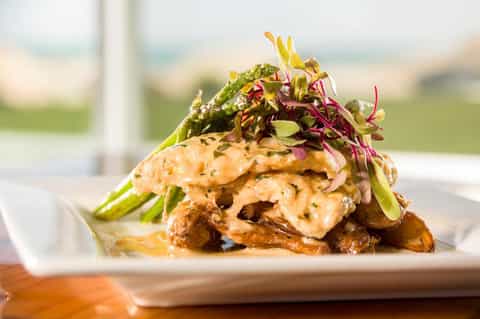 Plated seafood dish with greens and microgreens on white plate overlooking ocean