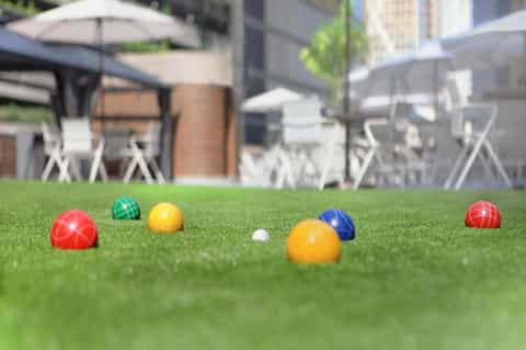 Bocce ball game setup on lawn with colorful balls and resort seating area with umbrellas