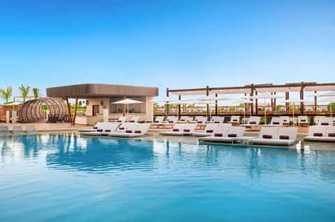 Resort pool area with loungers, pergola shade structures, and modern facilities