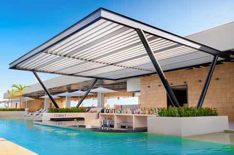 Modern poolside bar with retractable white louvered roof and turquoise pool beneath