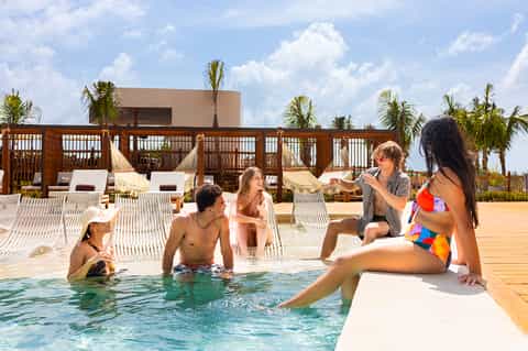 Resort pool with wooden deck, beachfront cabanas, and guests swimming in tropical setting