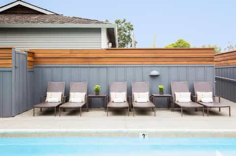 Row of lounge chairs with cushions beside residential pool and fenced yard