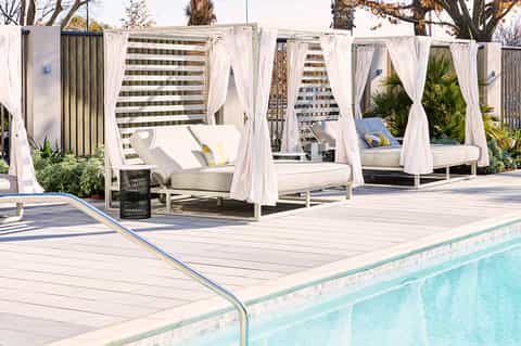 Outdoor pool deck with white cabanas and flowing curtains overlooking city skyline