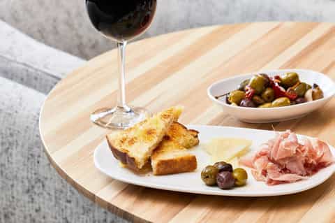 Wine glass, charcuterie board with cured meats, cheese, and olives on wooden table