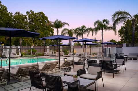 Upscale resort pool deck at dusk with lounge chairs, umbrellas, and palm trees