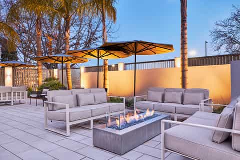 Luxury outdoor patio with fire pit, gray lounge seating, black umbrellas, and illuminated walls at dusk