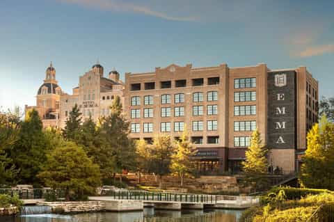 Historic brick hotel building with distinctive domed architecture beside a river with waterfall and green trees