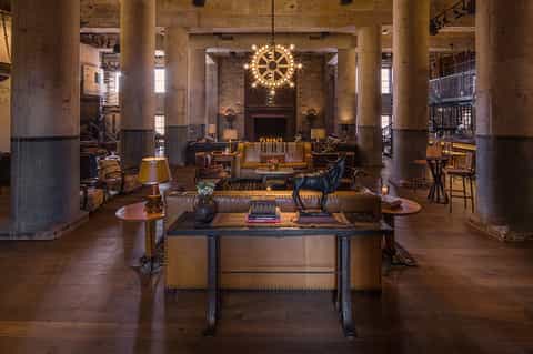 Grand hotel lobby with concrete columns, ornate gold chandelier, and vintage furnishings with warm lighting