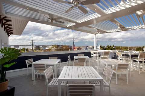 Rooftop dining area with white pergola, ceiling fans, tables, chairs, and waterfront views