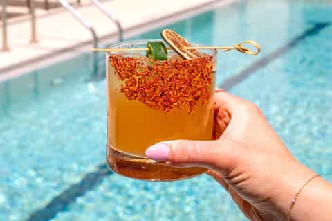 Cocktail with spiced rim and mint garnish held poolside with swimming pool background