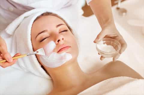 Spa therapist applying white facial mask to client with brush during beauty treatment