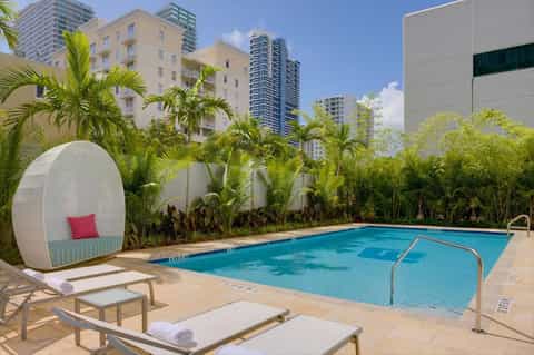 Resort pool surrounded by palm trees with white pod loungers and high-rise buildings in background