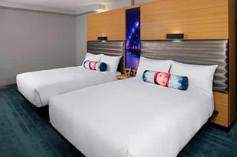 Hotel room with two queen beds, wood headboards, metallic accents, and decorative throw pillows