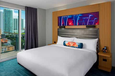 Modern hotel bedroom with king bed, wood accent wall, and city skyline view