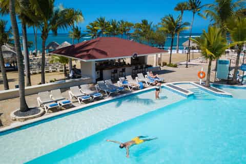 Beachfront resort pool with lounge chairs, bar, and ocean view with palm trees