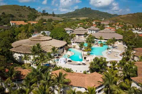 Aerial view of resort with turquoise pool, thatched-roof structures, and palm trees