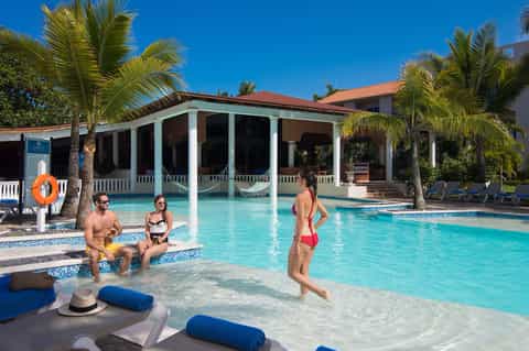 Tropical resort pool with guests in shallow water and pool house structure