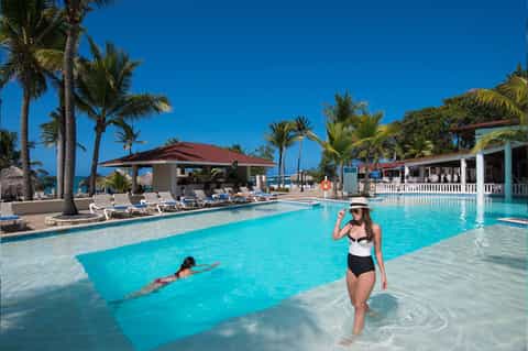 Tropical resort pool with crystal-clear turquoise water, palm trees, and beachfront loungers