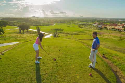 Couple playing golf on scenic hillside course with lush green landscape and mountain views