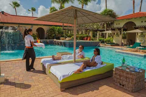 Resort pool area with lounge beds, umbrellas, and staff attending to guests