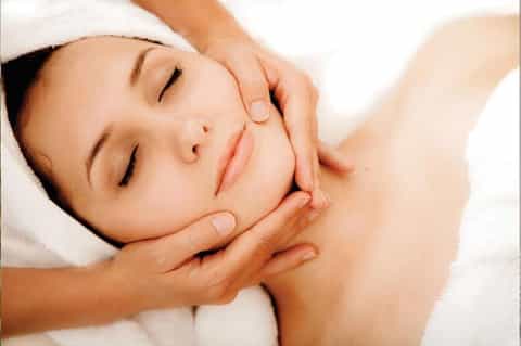 Woman receiving facial massage or spa treatment with eyes closed and white towel headwrap