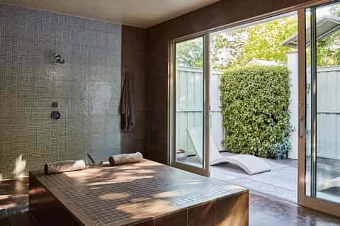 Luxurious spa bathroom with tiled soaking tub, glass shower, and access to private outdoor garden courtyard